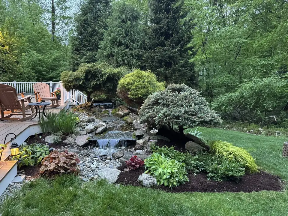 A boulder water feature beside a patio with mixed plantings